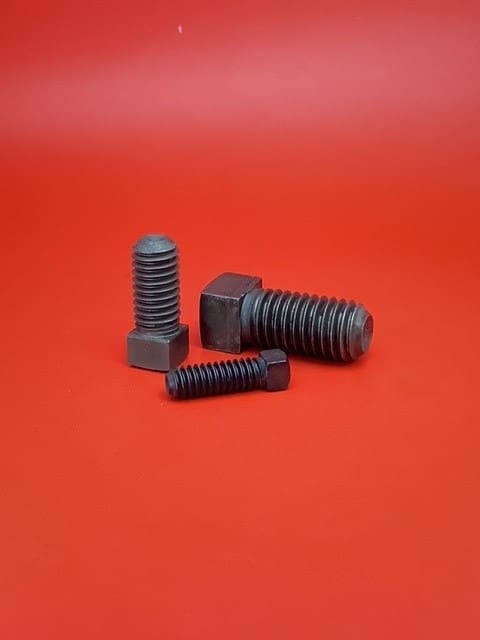 A group of four black nuts and bolts on top of a red surface.